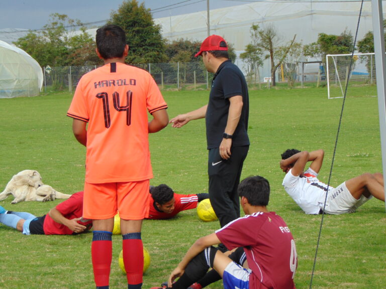 Entrenador da indicaciones a jóvenes futbolistas en la cancha de Casa Tibaná
