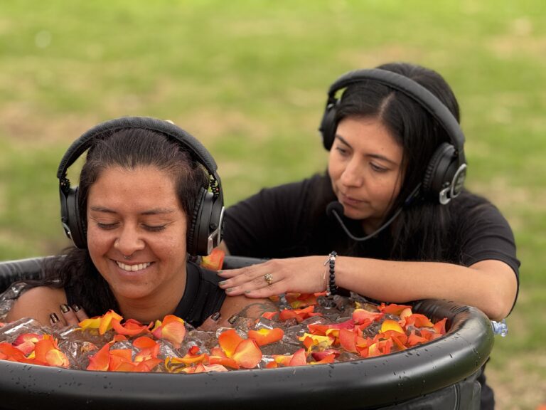 Participante en una tina de agua fría con pétalos acompañada por una facilitadora