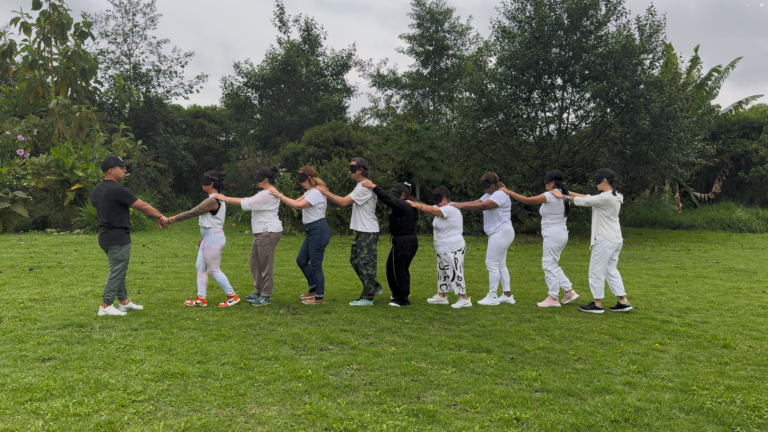 Grupo en fila con los ojos vendados guiado por un facilitador en el jardín